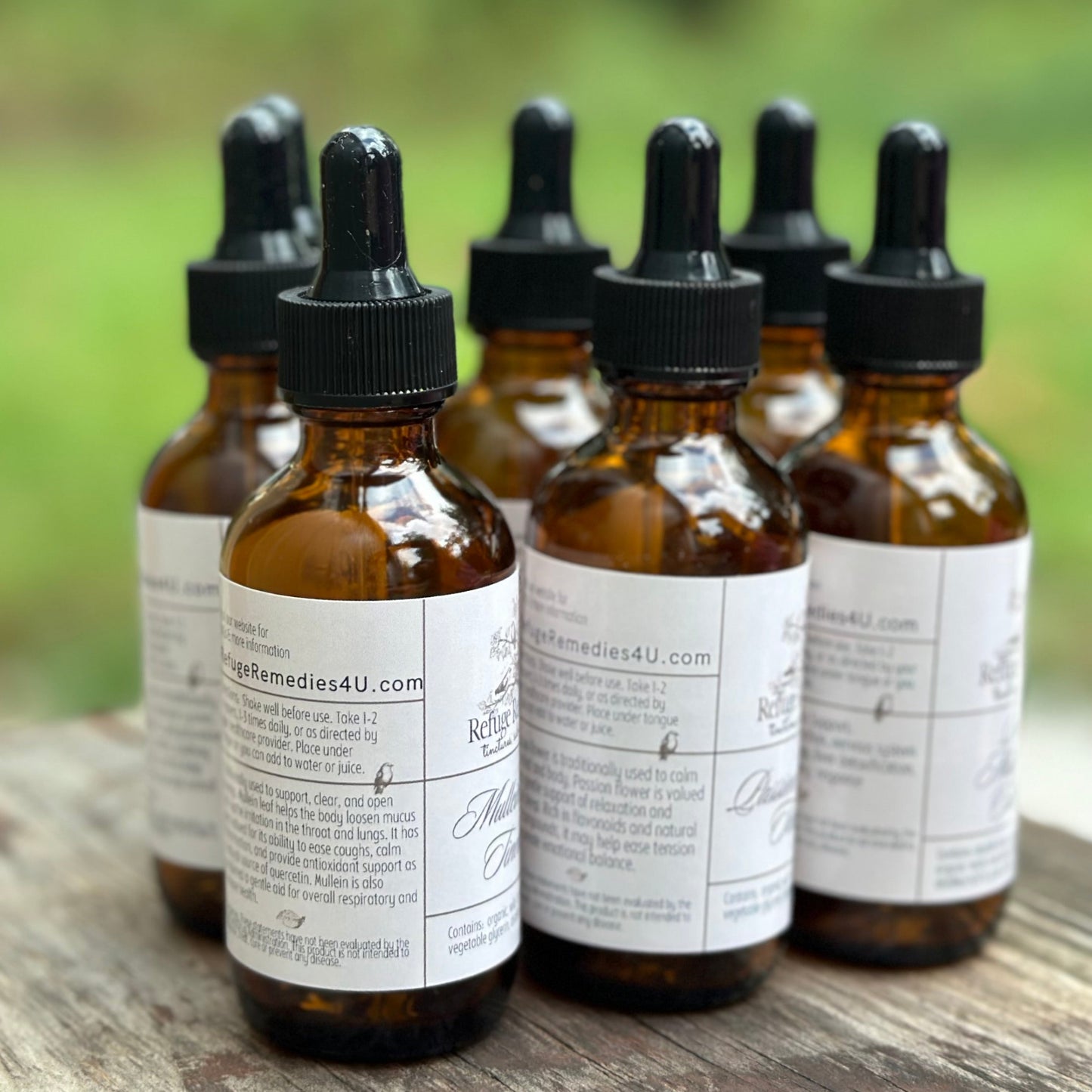 Set of brown glass bottles with dropper caps on a wooden surface with a blurred green background.